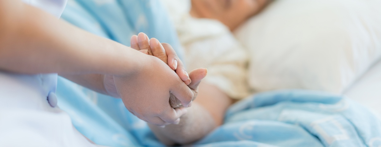 caregiver holding patient's hand on bed
