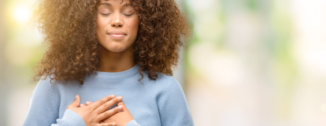 woman wearing a sweater smiling with hands on chest with grateful gesture on face