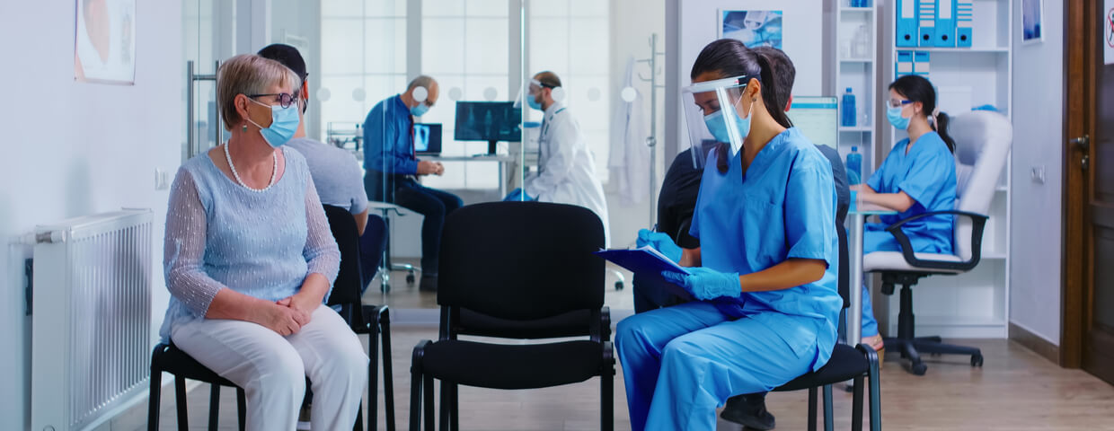 Nurse and senior patient in hospital examination room wearing mask against covid19