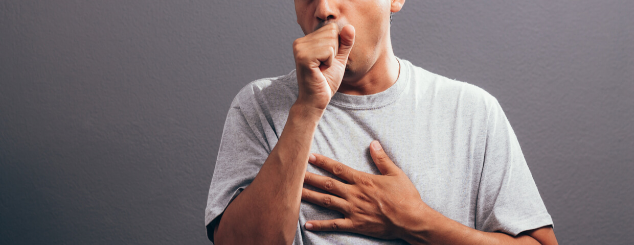 Man coughing into his fist, isolated on a gray background