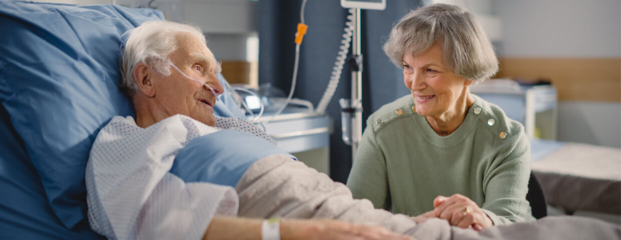 wife supporting husband as he recovers in hospital bed